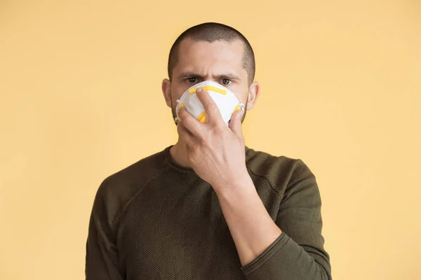 Caucásico hombre serio está usando y sosteniendo una máscara en su cara posando en una pared de estudio amarillo — Foto de Stock