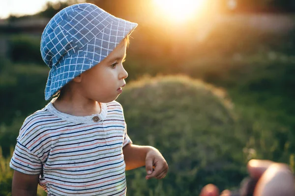 Yakın çekimde mavi şapkalı beyaz bir çocuk ailesinin yanında çimlerle bir tarlada yürüyor. — Stok fotoğraf