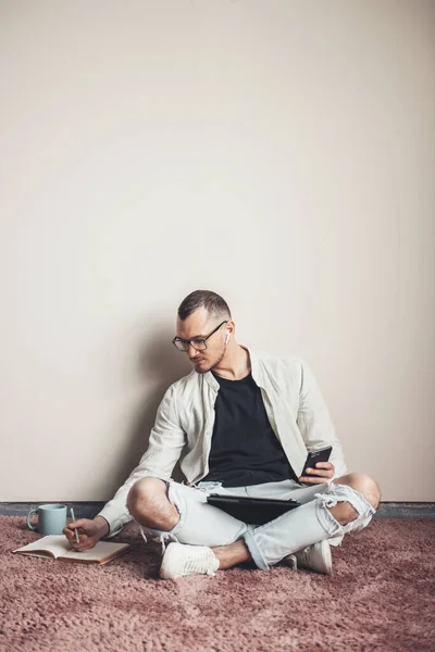 Συμπυκνωμένο freelancer χρησιμοποιώντας tablet και τηλέφωνο γράφουν εργασίας στο σπίτι στο πάτωμα έχοντας έναν καφέ — Φωτογραφία Αρχείου