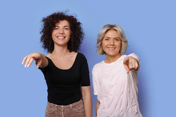 Due sorelle con i capelli ricci puntano la macchina fotografica sorridente in t-shirt su un muro di studio blu — Foto Stock