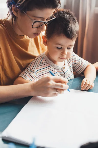 Close up foto de uma mãe caucasiana ajudando seu filho a escrever em casa — Fotografia de Stock