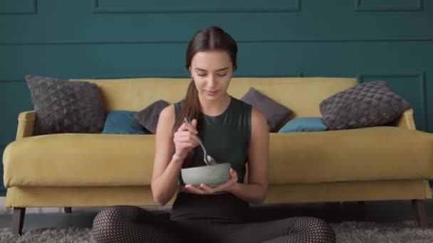 브루넷 여성 이 그릇을 들고 웃으며 바닥에서 건강 한 곡물을 먹고 있습니다 — 비디오