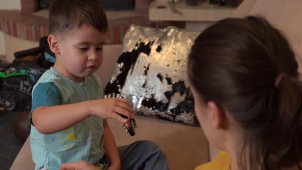 Liebenswert klein junge ist spielend mit ein spielzeug bike während mutter is watching him auf die couch — Stockvideo