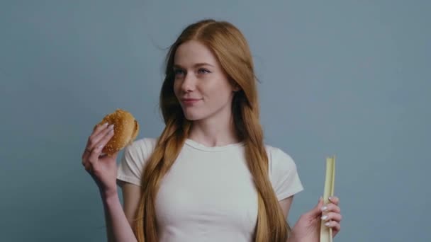 Mulher de gengibre com sardas está fazendo escolha entre fast food e natural segurando um hambúrguer e alho-porro — Vídeo de Stock