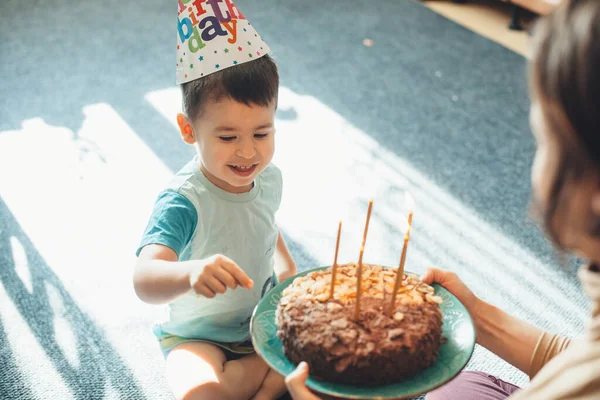 Urocze dziecko nosi kapelusz, podczas gdy matka daje mu tort urodzinowy. — Zdjęcie stockowe