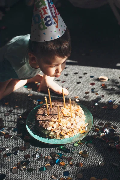 Kafkasyalı küçük bir çocuk parti şapkası takmış doğum gününü kutlarken pastadaki ışıkları söndürüyor. — Stok fotoğraf
