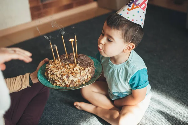 Criança adorável com chapéu de festa está soprando as luzes no bolo enquanto a mãe está segurando a placa — Fotografia de Stock