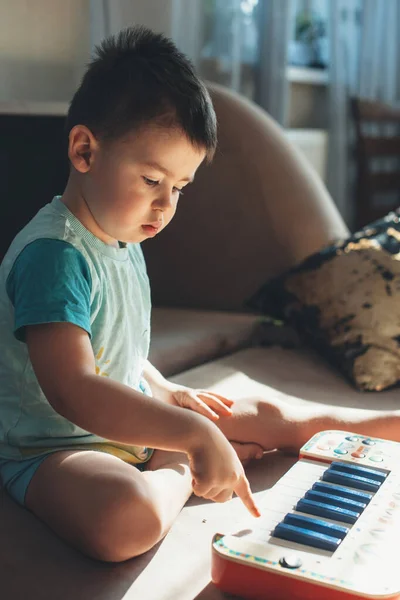 Caucasiano criança pequena está tentando jogar piano de brinquedo no chão — Fotografia de Stock