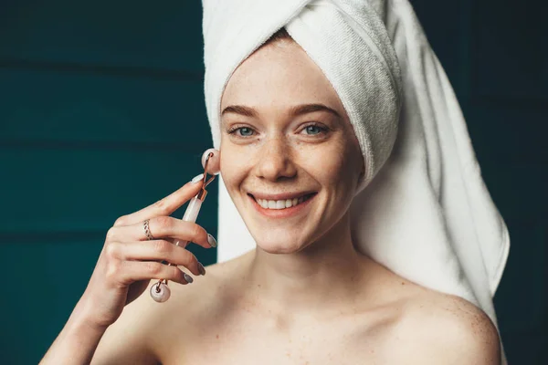 Vrouw met sproeten glimlachen op camera terwijl masseren haar gezicht met een derma roller — Stockfoto