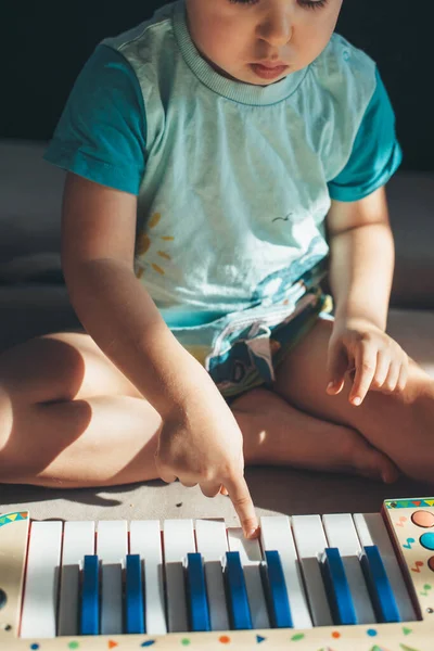 Close up photo of a small boy playing piano toy sitting on the floor concentrated