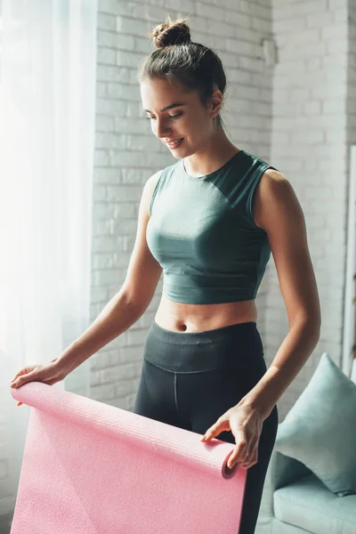 Donna felice sta finendo la sua sessione di allenamento di fitness raccogliendo il suo tappeto dal pavimento — Foto Stock