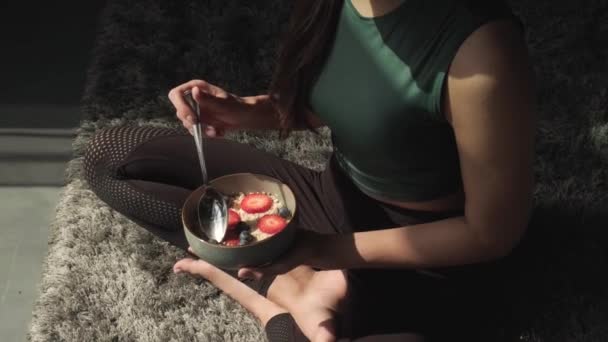 白人スポーティな女性は果物と床の上に座っている穀物を食べている — ストック動画
