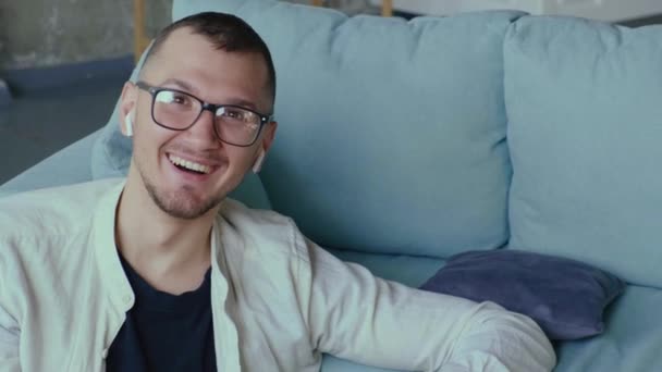 Sorrindo homem está olhando para a câmera através de óculos enquanto trabalhava a partir de casa remotamente — Vídeo de Stock