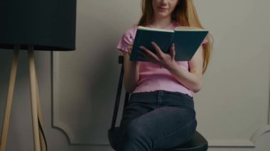 Çilli kızıl kadın evde oturmuş kitap okuyor.