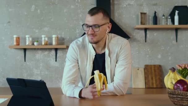 Mladý podnikatel jí banán, zatímco mluví během obchodního hovoru z kuchyně — Stock video