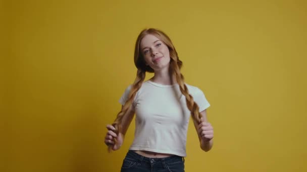 Pecosa mujer caucásica con el pelo rojo está fijando su cabello posando en una pared de estudio amarillo — Vídeos de Stock