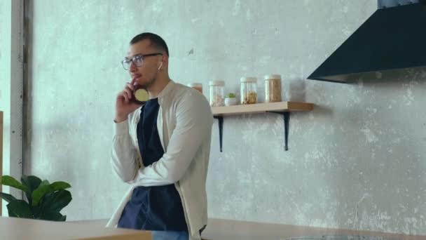 Jovem empresário caucasiano está comendo uma maçã enquanto trabalha em casa na cozinha — Vídeo de Stock