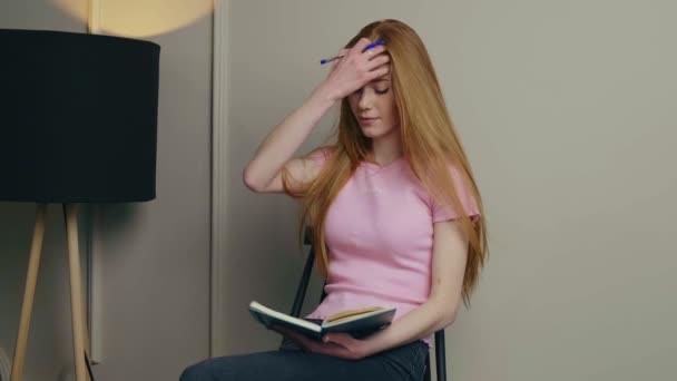 Ginger kobieta z piegami planuje coś podczas pisania w książce w domu — Wideo stockowe