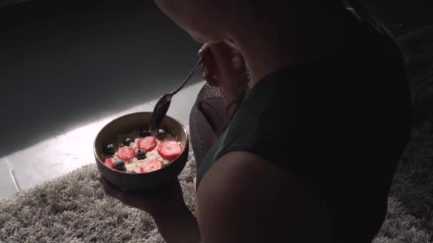 Video von einer Kaukasierin, die zu Hause auf dem Fußboden Getreide mit Milch und Früchten isst — Stockvideo