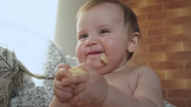 Close up vídeo de um pequeno bebê caucasiano comendo algo enquanto está sentado na cama — Vídeo de Stock