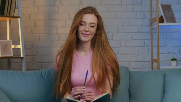Ginger kobieta uśmiecha się do kamery podczas rozmowy wideo w domu trzymając książkę i mówiąc — Wideo stockowe