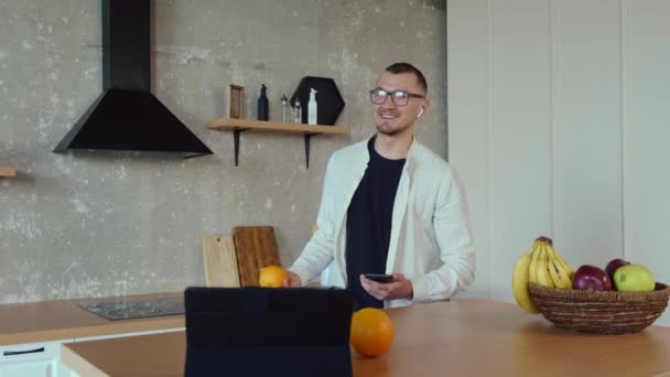 Blanke man eet fruit terwijl hij thuis op afstand op de tablet werkt — Stockvideo