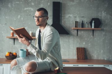 Genç girişimci mutfakta kahve içerken bir kitap okuyor.