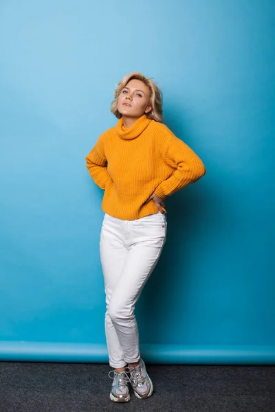 Mujer adorable con el pelo rubio rizado está posando en una pared de estudio azul — Foto de Stock