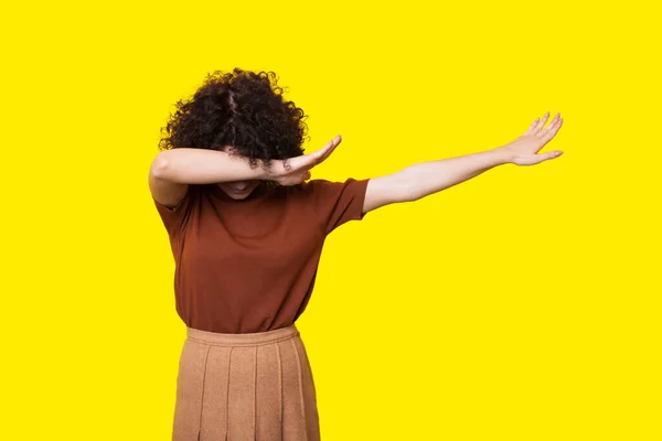 Femeia cu părul creț gestuează semnul dab pozând pe un perete galben al studioului — Fotografie, imagine de stoc