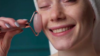 Close up video of a cheerful ginger woman with freckles massaging her face with a derma roller
