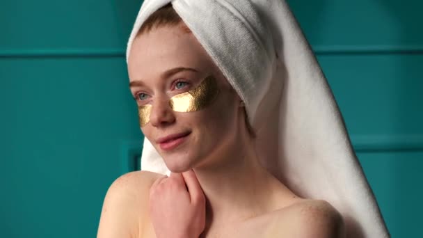 Adorable ginger woman with freckles is wearing golden eye patches after taking a shower — Vídeo de stock