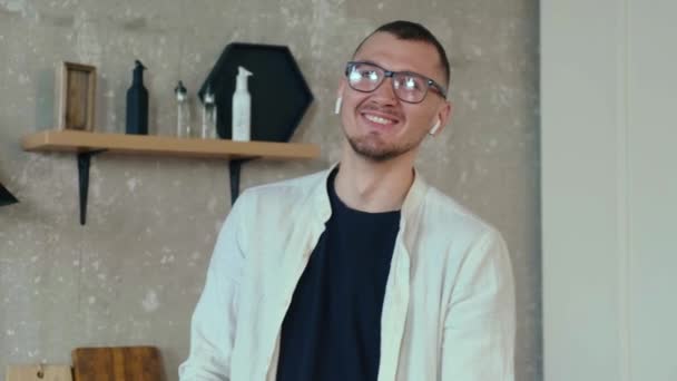 Sorrindo homem está usando fones de ouvido enquanto tendo uma chamada remotamente de casa — Vídeo de Stock