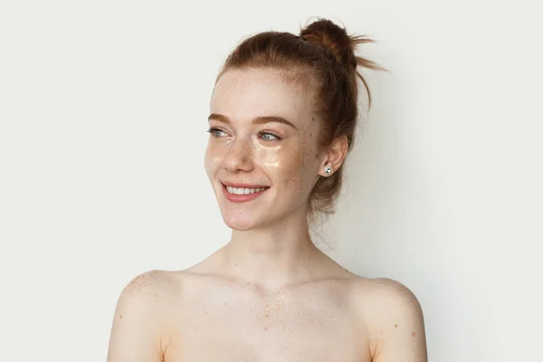 Adorable femme roux avec des taches de rousseur sourit sur un mur de studio blanc portant des patchs hydrogel yeux transparents — Photo
