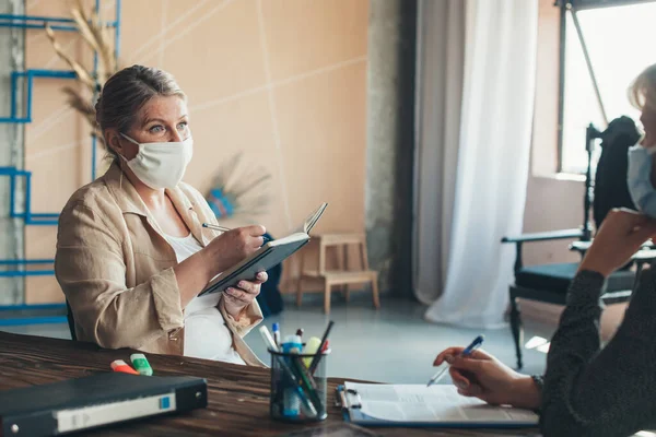 O femeie de afaceri blondă are o întâlnire cu un client de afaceri la birou purtând mască medicală — Fotografie, imagine de stoc