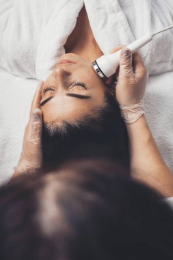 Güzellik salonunda özel aletlerle yüz masajı yapan bir kadının fotoğrafı.