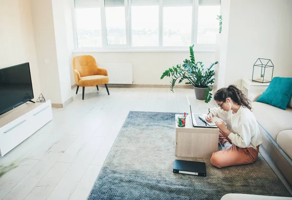 Estudiante de pelo rizado concentrado está haciendo la tarea en el escritorio sentado en el suelo en casa — Foto de Stock