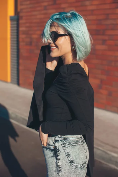 Blå hårig kvinna ler utanför håller sin jacka bär glasögon — Stockfoto
