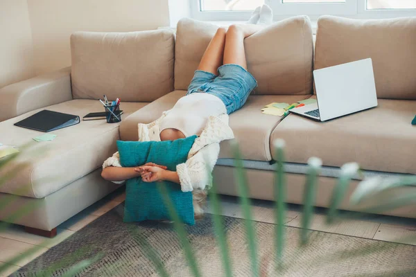 Cansada mujer caucásica está acostada en un sofá mientras hace la tarea con un ordenador portátil — Foto de Stock