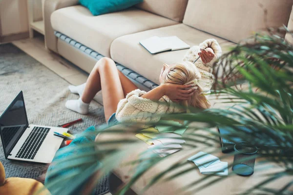 Bakåt visa foto av en blond dam som ligger nära soffan på golvet gör läxor på laptop — Stockfoto