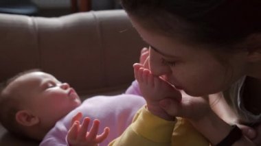 Newborn baby lying on the couch while mother is kissing her feet and playing with her