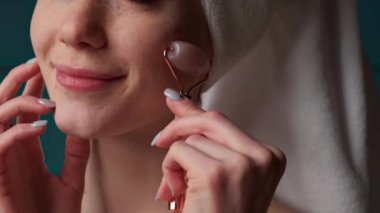 Close up video of a woman with freckled face applying pink derma roller on face smiling at camera