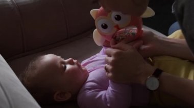 Adorable and careful mother is playing with her newborn baby showing her a toy while putting to sleep