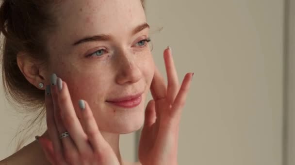 Ginger caucasian woman is massaging her face smiling while applying anti aging cream — Vídeo de stock