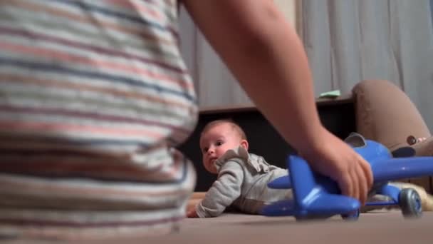 Back view video of a small kid playing with little sister on the couch with plastic toys — Vídeos de Stock