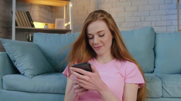 Adorable ginger woman is working remotely on a tablet from home using a phone sitting on the floor — Stock Video