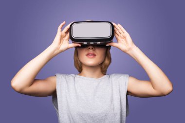 Menekşe arka plandaki sarışın kadın yeni bir VR kulaklık takıyor. İlk kez test ediyor.