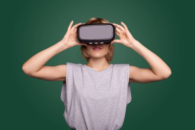 Yeşil duvardaki sarışın kadın yeni ekran denemesi yaparken gülümsüyor.