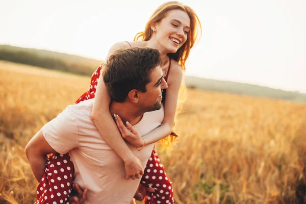 Adorabile coppia stanno giocando in un campo durante un tramonto sorridente e abbracciando — Foto Stock