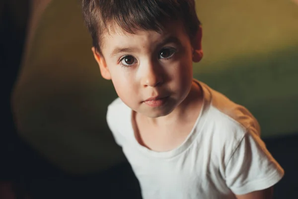 Kanepenin yanında oynarken kameraya bakan esmer bir çocuğun yakın fotoğrafını çek. — Stok fotoğraf