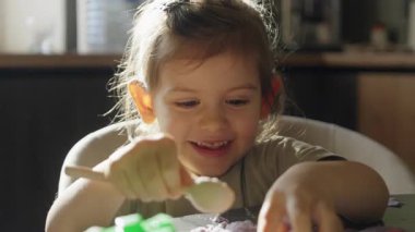 Mutfak masasında parlak ışıklandırmayla yaratıcı duygusal oyunlar oynayan neşeli genç bir kız.